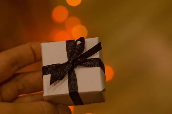 Petit cadeau de Noël ou Nouvel An avec ruban noir à portée de main sur fond bokeh bleu nuit. Petit concept de cadeau fait à la main . — Photo