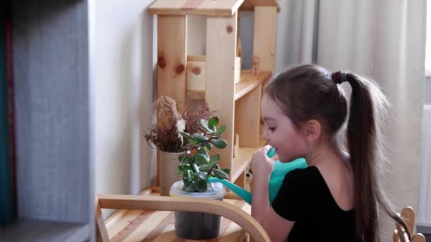 Μικρό κορίτσι κρατώντας πότισμα μπορεί να το νερό σπίτι φυτό στην κατσαρόλα. Η μικρή κόρη βοηθάει τη μαμά. Νεαρή κοπέλα νοιάζεται για τα λουλούδια — Αρχείο Βίντεο