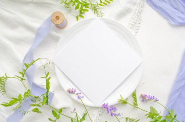 Beyaz arka planda menekşe çiçekleri ve ince ipek kurdeleli bir düğün modeli. Tebrik kartı ya da kenarları sivri düğün davetiyesi. Düz yatıyordu, üst