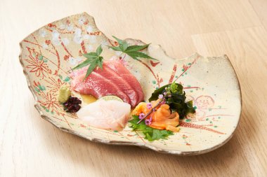 Ahşap zemin üzerinde seramik tabakta yenilebilir çiçeklerle süslenmiş kaliteli saşimi.