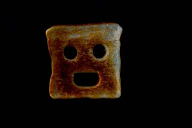 Piece of toast with a human face carved into it isolated on a black background image with copy space in landscape format clipart