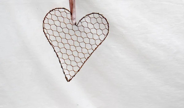 Wire heart hanging from a pink ribbon isolated against a white cloth background image with copy space in landscape format