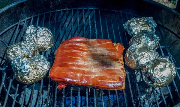 红色的肉和土豆包裹在箔慢慢烹饪在一个户外水壶烤箱图像与复制空间在景观格式 — 图库照片