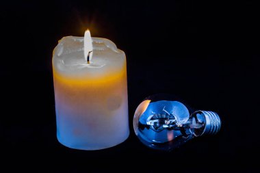 Burning candle and an electric light globe isolated on a black background image with copy space in landscape format clipart
