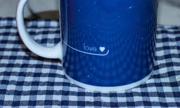 A blue and white ceramic mug with a love theme isolated on a blue and white table cloth image with copy space in landscape format