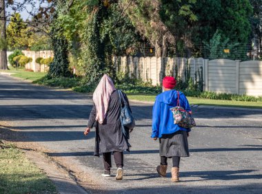 Johannesburg, Güney Afrika - 17 Mayıs 2019: Kimliği belirsiz iki siyah kadın öğleden sonra ev işlerinden eve yürürken, fotokopi alanı ile manzara formatında şehir görüntüsünde hizmetçi olarak