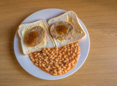 Two slices of white bread with soya patties on them and baked beans on a white plate form the shape of a face on a wooden table in landscape format with copy space clipart