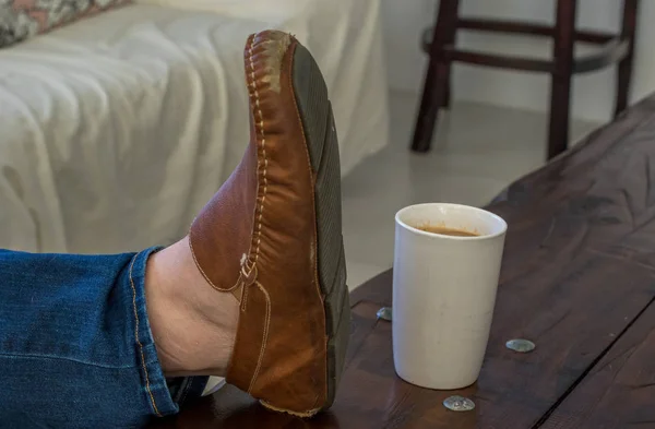 A mans feet on a table next to a cup of coffee