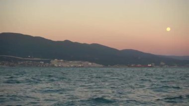 Büyük liman kenti üzerinde yükselen dolunay.
