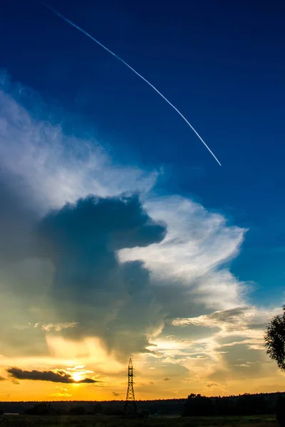 Beautiful bright sunset against a blue sky with clouds and a bright condensation trail from an airplane