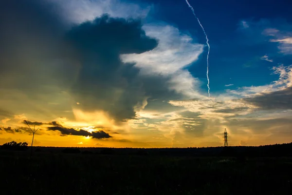 Beautiful bright sunset against a blue sky with clouds and a bright condensation trail from an airplane