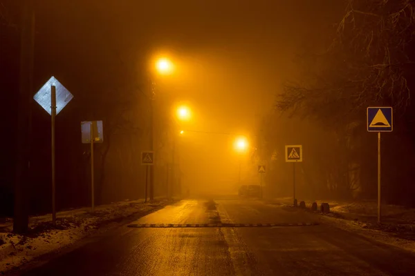 The road at night illuminated by dim lanterns during a thick fog