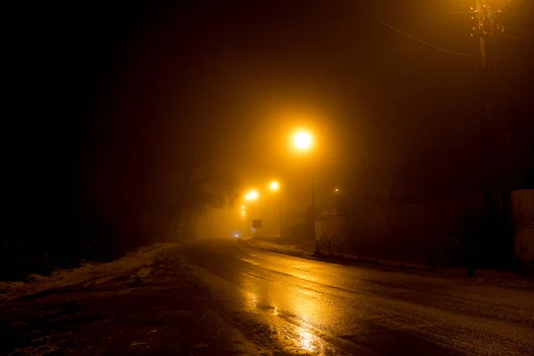 濃い霧の中に薄暗いランタンに照らされた夜の道 — ストック写真