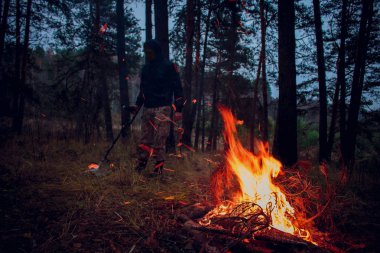 Doğada, arka planda bir ateşten bir metal dedektörü ile arama