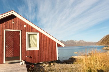 Ahşap Norveç plaj kulübe taşlarla görünümünü Tromso fiyort, Arctic Circle, Norveç ve dağ tepe bir güneşli mavi gökyüzü gün bakan kıyı üzerinde
