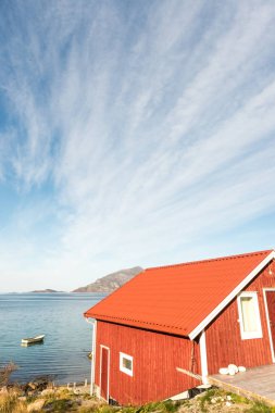 Ahşap Norveç plaj kulübe taşlarla görünümünü Tromso fiyort, Arctic Circle, Norveç ve dağ tepe bir güneşli mavi gökyüzü gün bakan kıyı üzerinde