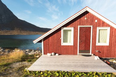 Ahşap Norveç plaj kulübe taşlarla görünümünü Tromso fiyort, Arctic Circle, Norveç ve dağ tepe bir güneşli mavi gökyüzü gün bakan kıyı üzerinde