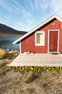 Ahşap Norveç plaj kulübe taşlarla görünümünü Tromso fiyort, Arctic Circle, Norveç ve dağ tepe bir güneşli mavi gökyüzü gün bakan kıyı üzerinde