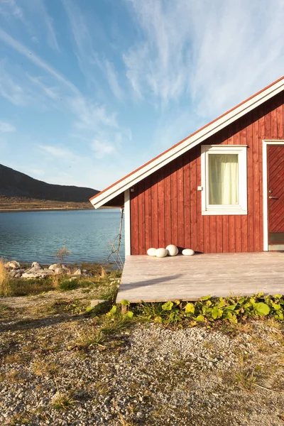 Ahşap Norveç plaj kulübe taşlarla görünümünü Tromso fiyort, Arctic Circle, Norveç ve dağ tepe bir güneşli mavi gökyüzü gün bakan kıyı üzerinde