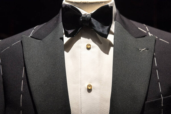 Close up on top part of tailored jacket on mannikin with black bow tie and sequined buttons on shirt