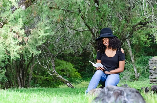 Una joven negra de entre 20 y 30 años sentada leyendo un libro sola, en un parque — Foto de Stock