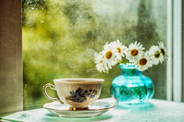 Pencere kenarında sıcak çay ve bir buket papatya