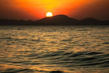 Denizin üzerinde tropik turuncu gün batımı. Güneş dağların arkasında batar. Tayland