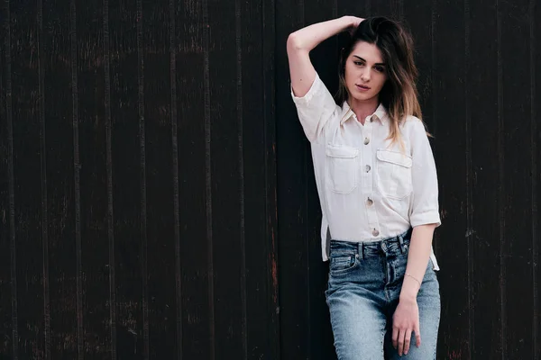 Una giovane hipster bella donna con lunghi capelli castani in estate con jeans in denim con uno sfondo marrone — Foto Stock