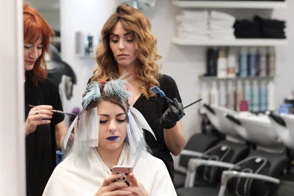 Två unga Frisör färgning hår av kvinnlig klient medan hon ser till sin mobil — Stockfoto