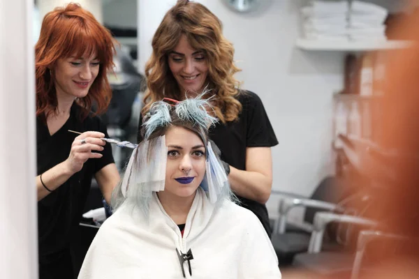 Dos peluquero joven teñir el pelo de cliente femenino mientras ella está sentada en la silla —  Fotos de Stock