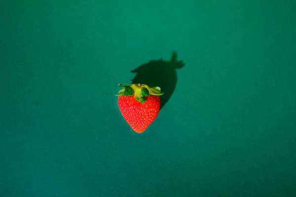 a single strawberry with a heart shape in a strong green background
