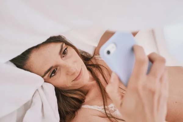 Eine junge Frau in Unterwäsche auf ihrem Bett mit einem Handy — Stockfoto