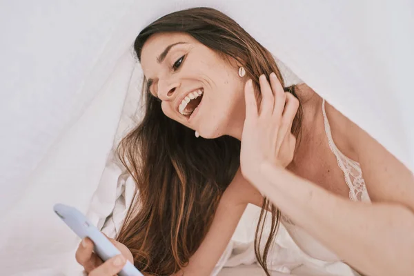 Eine junge Frau in Unterwäsche auf ihrem Bett mit einem Handy — Stockfoto