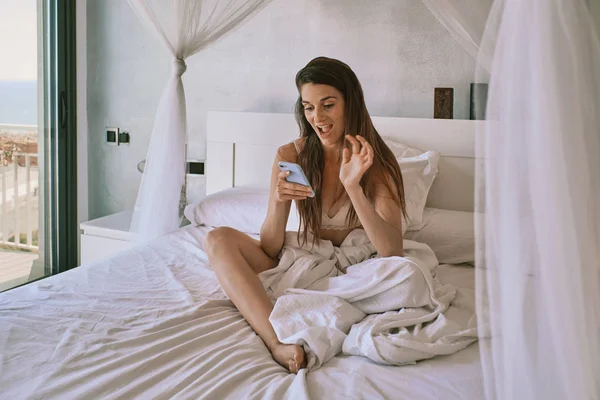 Una giovane donna in biancheria intima sul suo letto utilizzando un telefono cellulare — Foto Stock