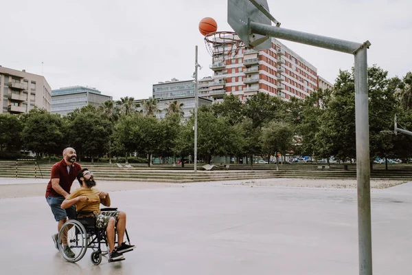 Un hombre discapacitado en silla de ruedas juega al basket con un amigo —  Fotos de Stock