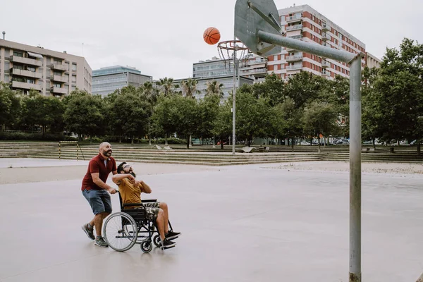 Un hombre discapacitado en silla de ruedas juega al basket con un amigo —  Fotos de Stock