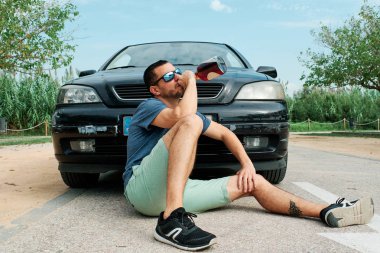 Sarhoş genç bir adam arabasının önünde içki içiyor - bağımlılık sorunu