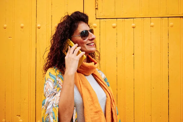 Een jonge vrouw met een mobiele telefoon met een sterke gele achtergrond — Stockfoto