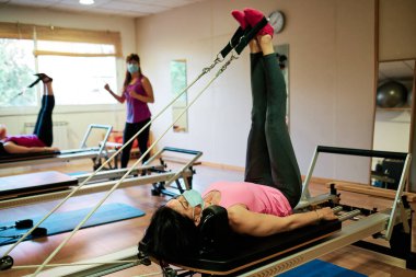 Egzersiz yapan bir grup olgun kadın, sosyal mesafeli Pilates ve Yoga yapıyor ve yüz maskesi takıyor.