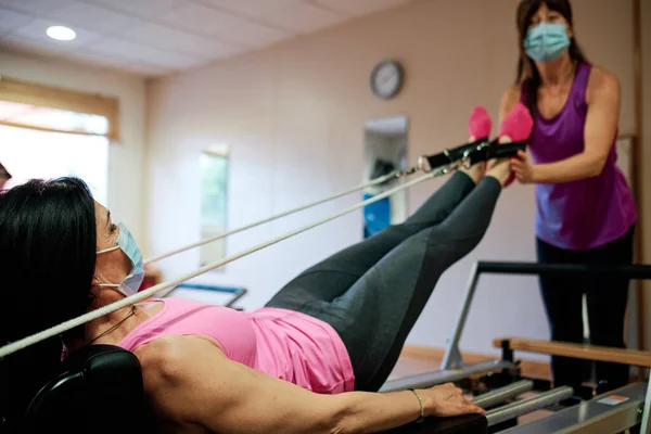 Egzersiz yapan bir grup olgun kadın, sosyal mesafeli Pilates ve Yoga yapıyor ve yüz maskesi takıyor.