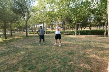 Ilık yaz gününün ve hareketli doğanın tadını çıkarırken parkta birlikte esneyen iki genç adam antrenman rutinlerine hazırlanıyorlar.