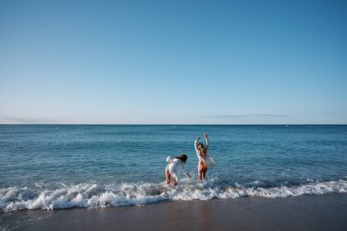 Kolları havada iki olgun kadın güneşli bir günde sahilde dalgaların ve okyanusun tadını çıkarıyorlar.