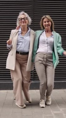 Olgun iş kadınları çağdaş şehir binasının önünde neşeli bir şekilde dans ediyor, profesyonel başarıyı enerjik ve oyuncu bir hareketle kutluyorlar.