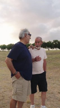 İki kıdemli adam bir tarlada birlikte yürüyor, öğleden sonra yürüyüşü sırasında birbirlerine eşlik ederek eğleniyorlar.