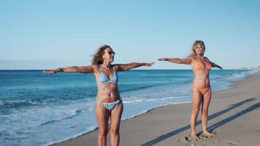 Olgun bir kadının güneşli bir plajda kol esneme egzersizi yaptığı yavaş çekim videosu.