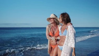 Bikini ve plaj kıyafetleri giyen iki neşeli son sınıf öğrencisi sahilde yürüyor ve birlikte kaygısızca vakit geçiriyorlar.
