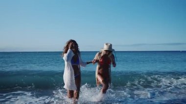 Bikini giyen ve plaj örtüsü takan iki olgun kadın sahilde koşuyor, tatillerinin tadını çıkarıyorlar.