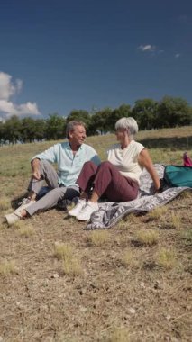 Yaşlı çift battaniyenin üzerinde dinleniyor, güneşli bir alanda hikayeler ve kahkahalar paylaşıyor, yavaş çekimde çekiliyor.