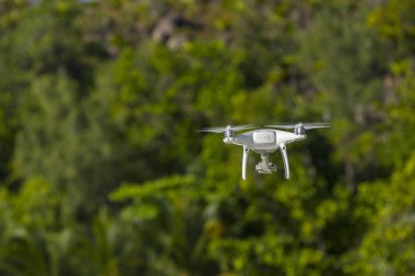 Uçan İHA, arka planda yeşil ağaçlar, İHA 'ya seçici odaklanma. 