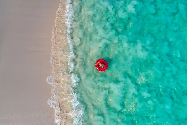 Aerial view of slim woman swimming on the swim ring  donut in the transparent turquoise sea in Seychelles. Summer seascape with girl, beautiful waves, colorful water. Top view from drone